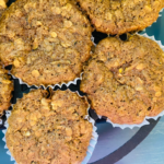 Whole Grain Zucchini Chocolate Chip Oatmeal Muffins fresh out of the oven in a cast iron muffin tin, sitting on a blue surface.