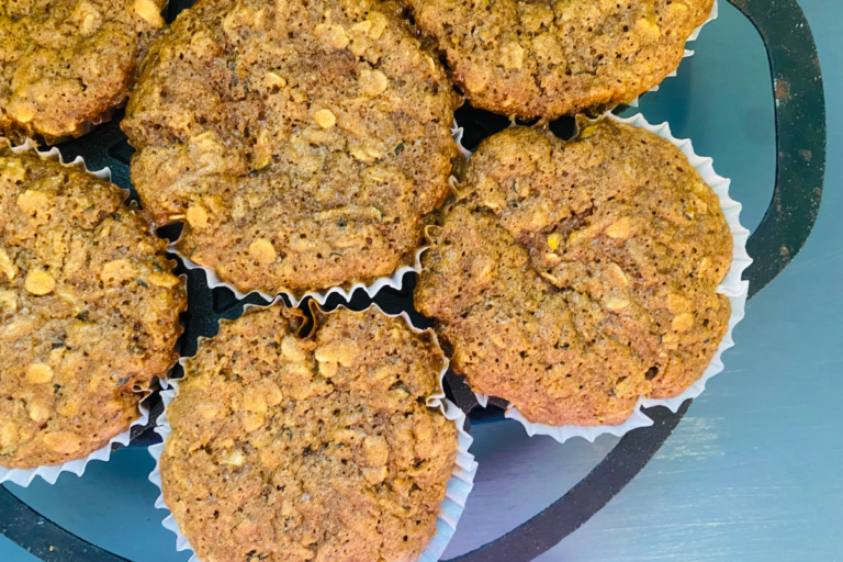 Whole Grain Zucchini Chocolate Chip Oatmeal Muffins fresh out of the oven in a cast iron muffin tin, sitting on a blue surface.