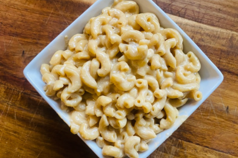 A bowl of Best Healthy Instant Pot Mac and Cheese in a white square bowling sitting on a wooden cutting board. You should make this recipe!