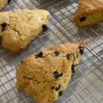 Freshly Milled Lemon Blueberry Scones sitting on a cooling rack getting lemon glaze drizzled on it.
