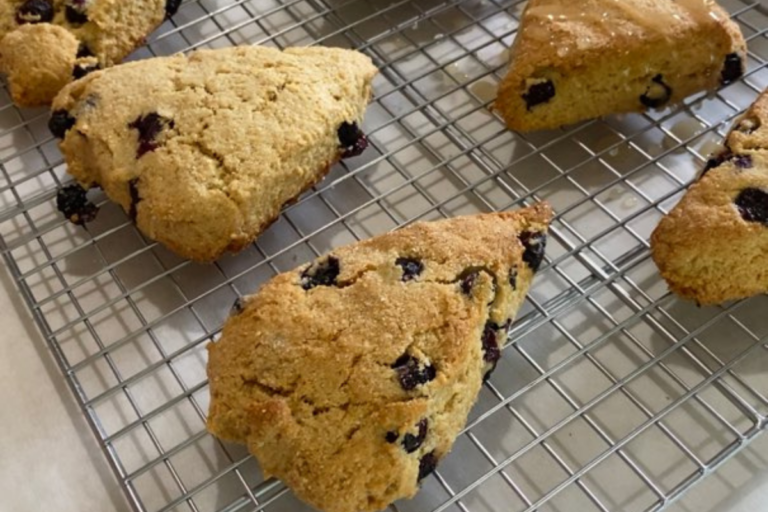 Freshly Milled Lemon Blueberry Scones sitting on a cooling rack getting lemon glaze drizzled on it.